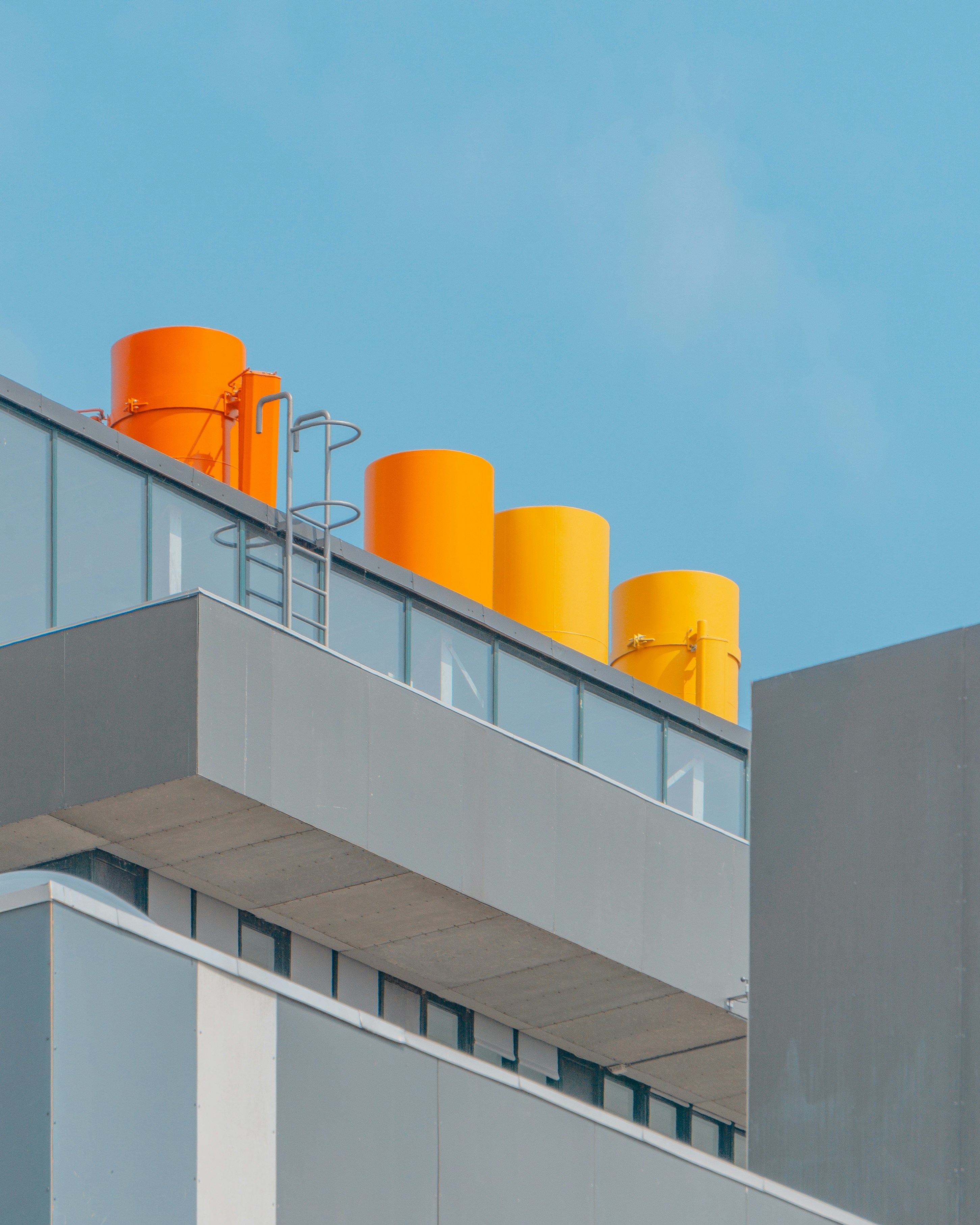 Modern industrial building with a minimalist design, featuring large gray panels and four brightly colored cylindrical rooftop structures in shades of orange.