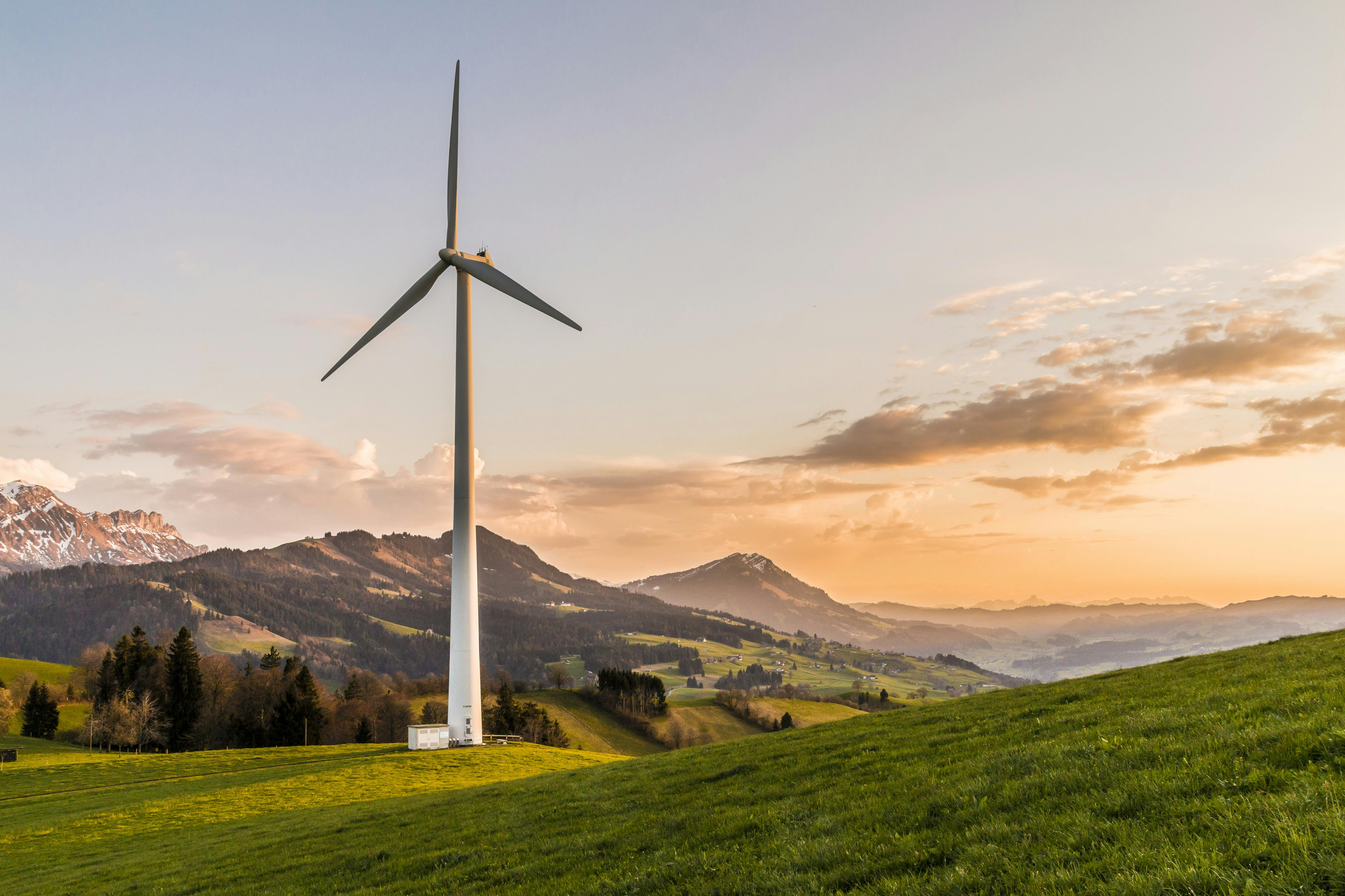 Wind turbine on a grassy hill with mountains at sunset.