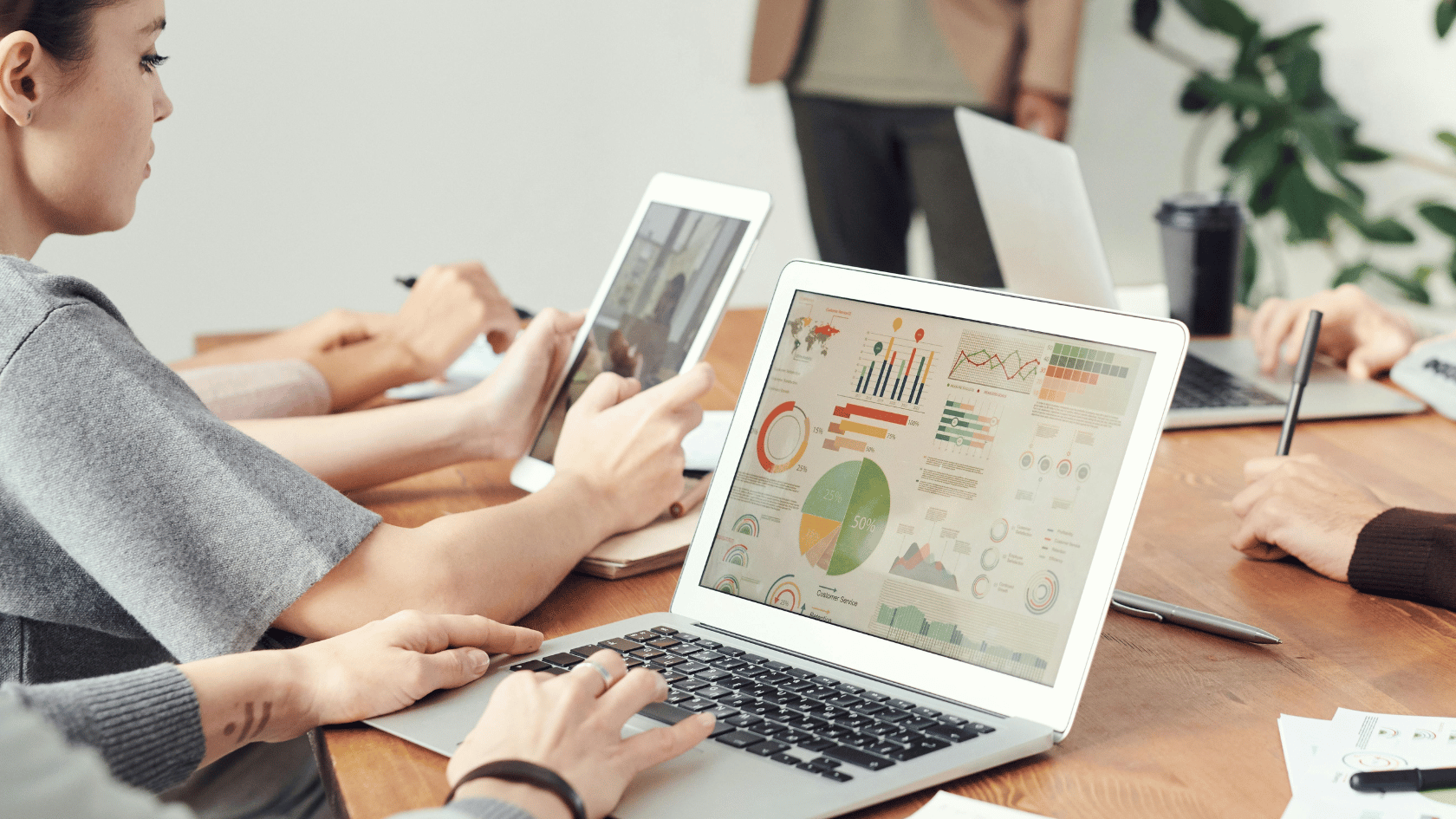 Group of people at a meeting table working on laptops and tablets displaying charts and graphs.