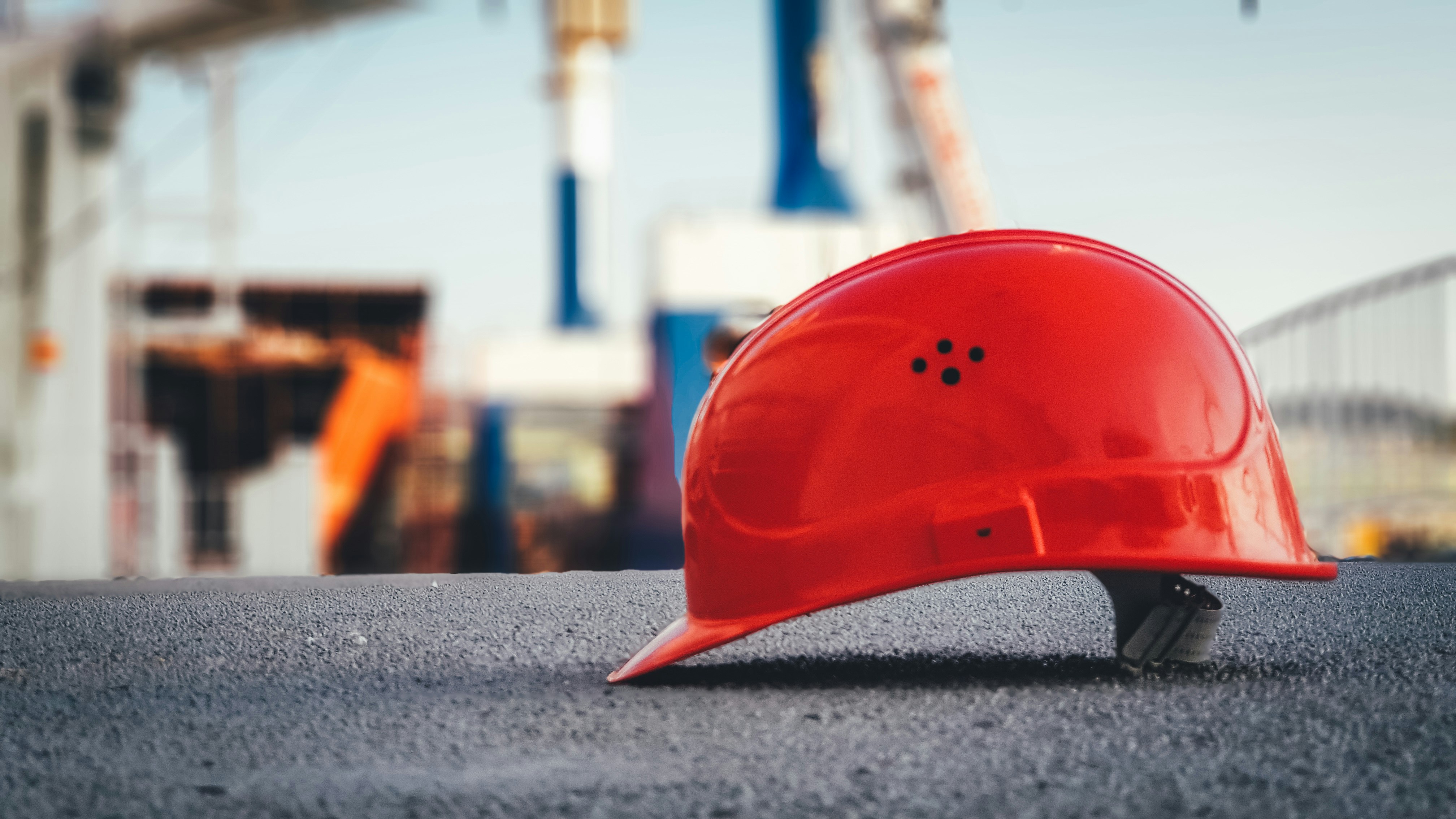 A bright red construction safety helmet is resting on a paved surface at a construction site.