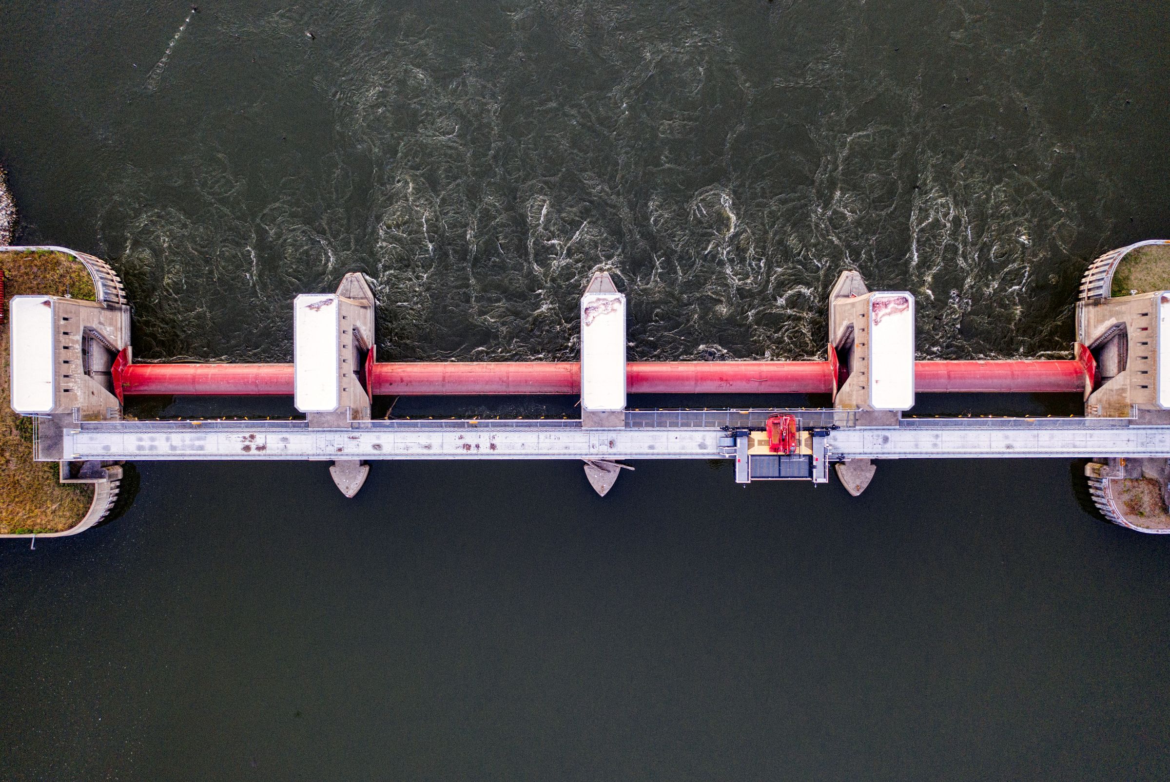 Aerial view of a hydroelectric dam with a red penstock crossing dark water