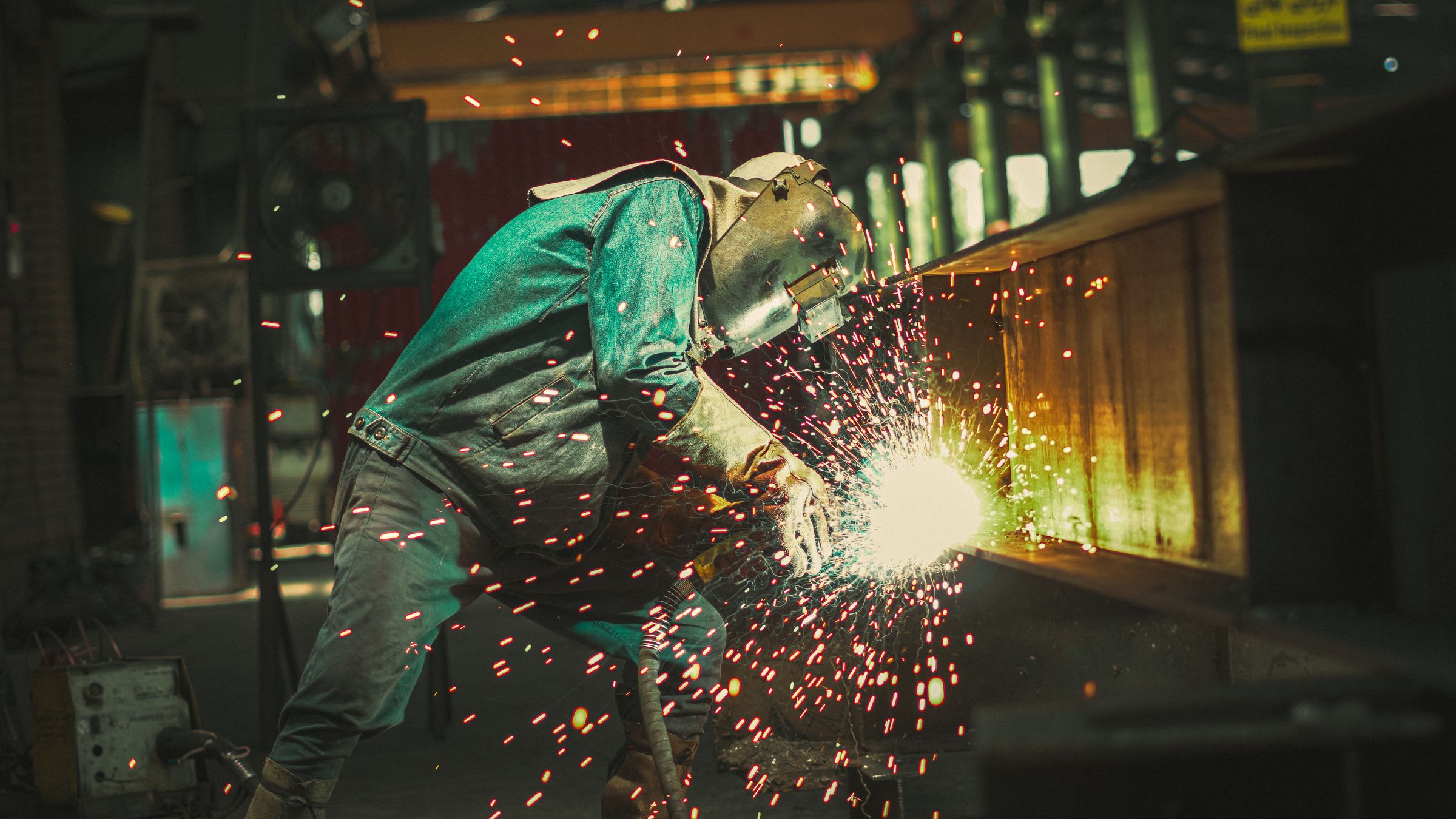 Welder in PPE grinding steel, sparks flying, in a fabrication shop